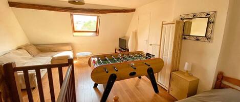 Una habitación acogedora con cama, mesa de futbolín, escritorio con lámpara y ventana que deja entrar luz natural.