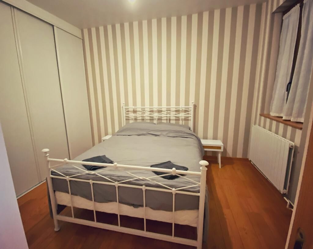 A single bed with a metal frame, a bedside table, and a radiator in a room with striped wallpaper.