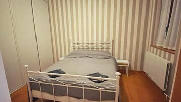 A single bed with a metal frame, a bedside table, and a radiator in a room with striped wallpaper.