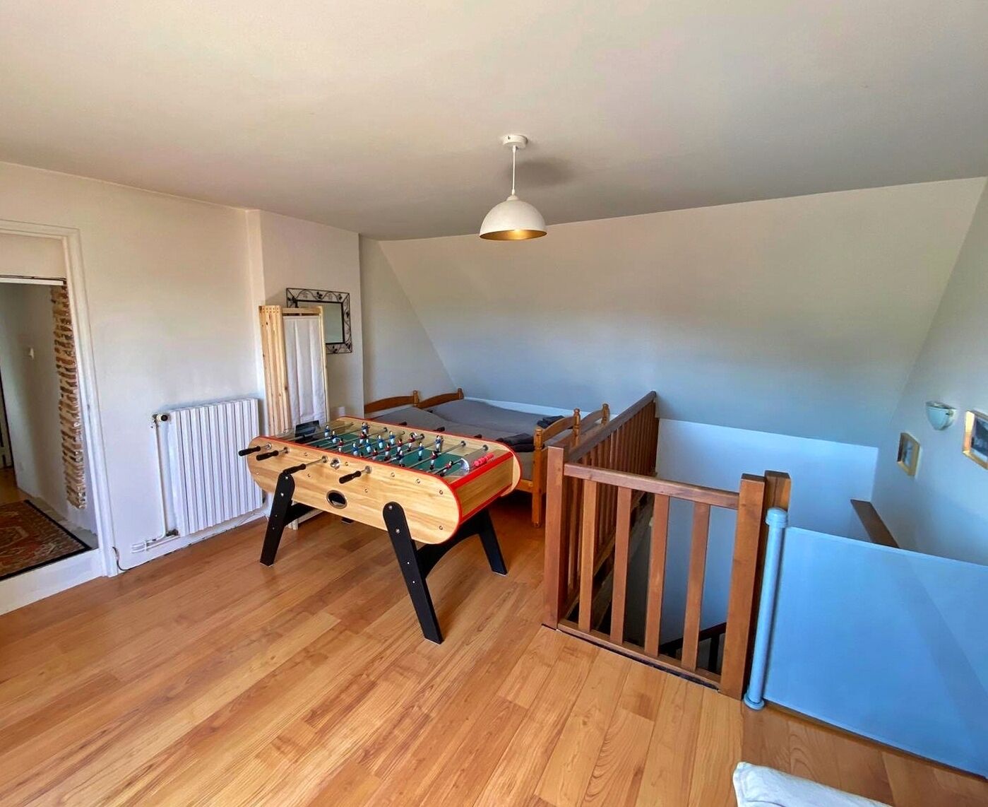 Una habitación con mesa de fútbol, cama de madera, radiador y luz en el techo.