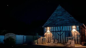 Ein Haus bei Nacht mit Pool, Holzterrasse und zwei Liegestühlen.