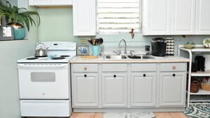 Una cocina con armarios blancos, estufa, fregadero y ventana con persianas.