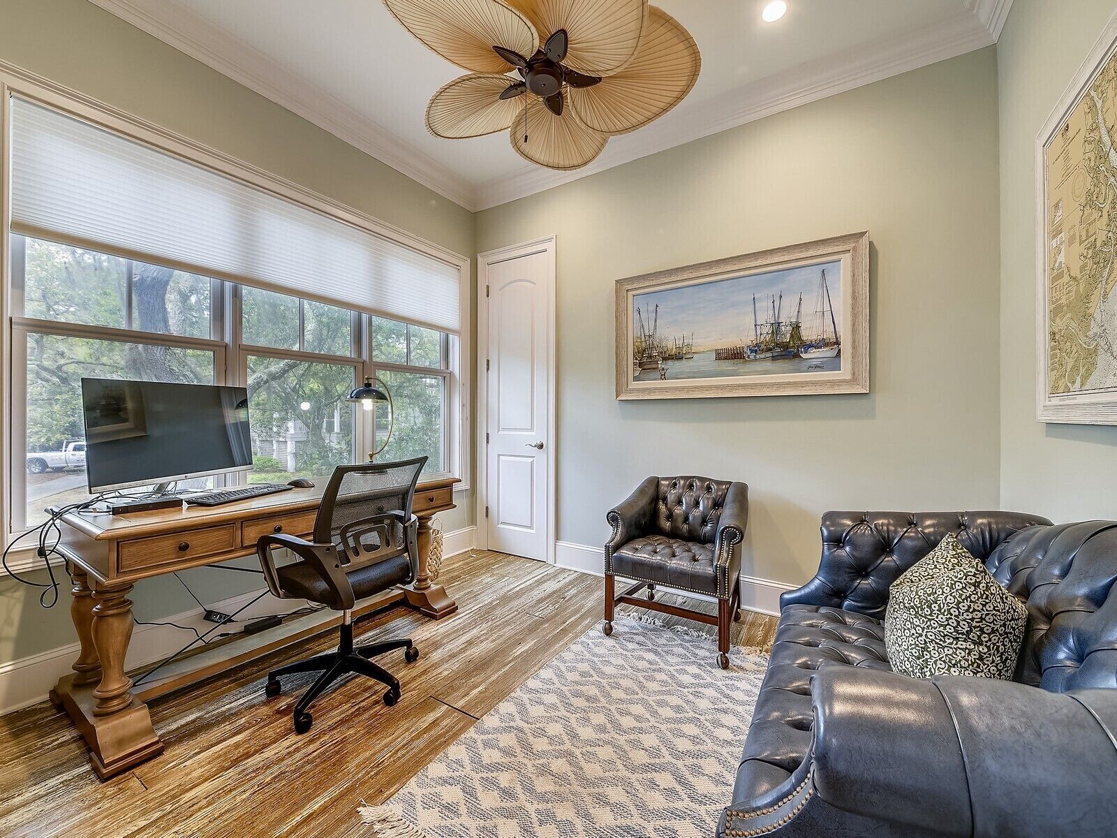 A room with a wooden desk, computer, and office chair, a leather sofa, and a ceiling fan.