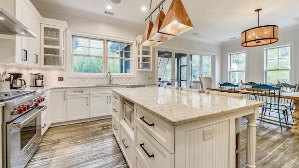 A spacious kitchen with white cabinetry, a large island, and a dining area with a wooden table and chairs. - Beautiful 2nd Row Beach Home w/ Beautiful Views (Hilton Head Island)