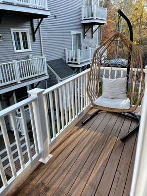 A wooden deck with a wicker swing chair and white railings. - Modern 30-bedroom townhouse parking on premises (north andover)