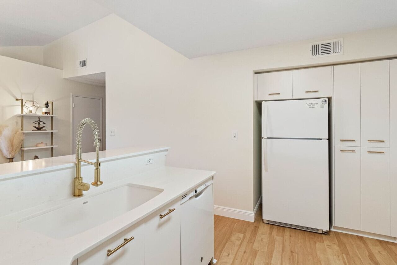 A modern kitchen with white cabinetry, a stainless steel refrigerator, and a gold faucet.