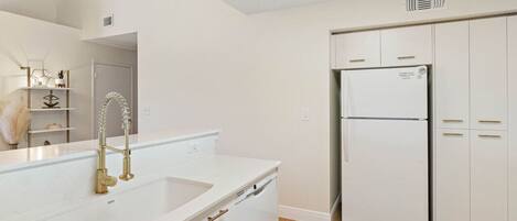 A modern kitchen with white cabinetry, a stainless steel refrigerator, and a gold faucet.