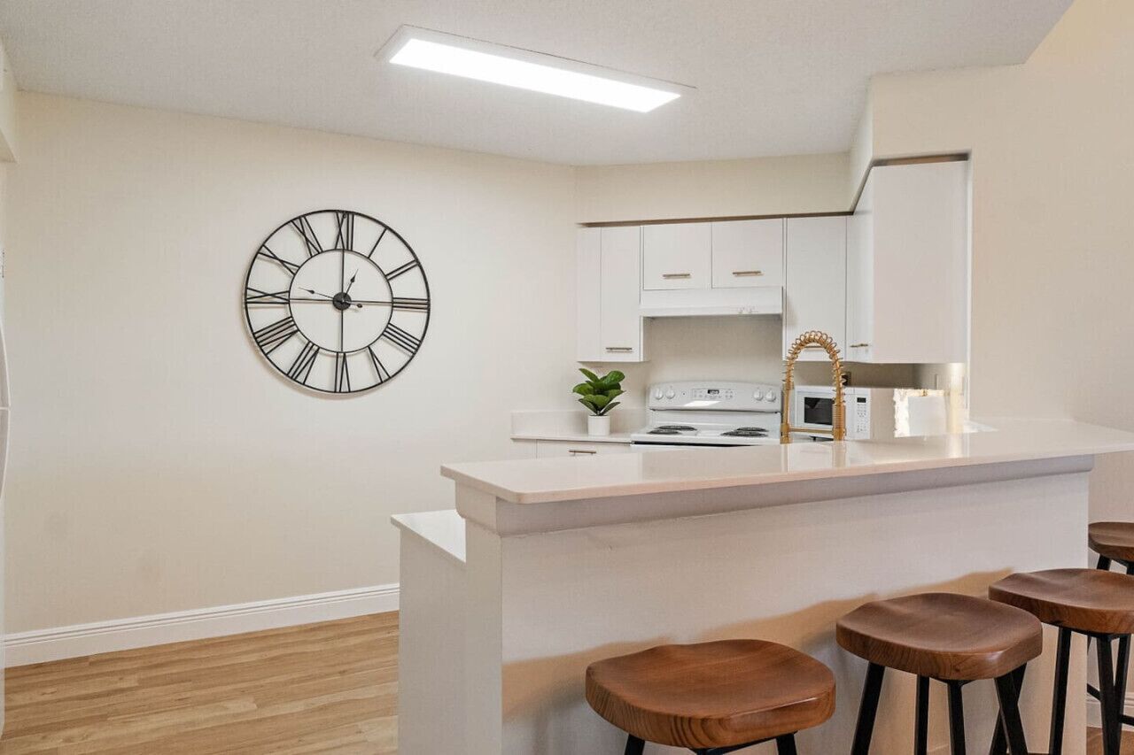 A modern kitchen with a central island, bar stools, a clock, and white cabinetry.