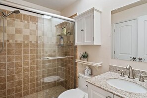 A bathroom with a glass-enclosed shower, a white toilet, a sink with a granite countertop, and a mirror above the sink. - Gorgeous Updated 2 Bedroom Lake View Unit in (Isla Del Sol)