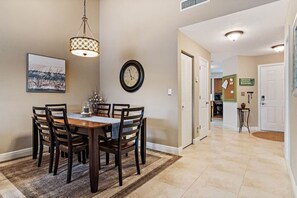A dining area with a wooden table, chairs, a clock, and a pendant light. - Gorgeous Updated 2 Bedroom Lake View Unit in (Isla Del Sol)