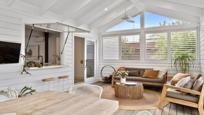 A spacious room with a wooden dining table, white chairs, a sofa, and a ceiling fan. - Breezy Beach Vibes 350m from Shore (Torquay)