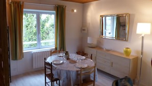 A dining area with a round table set for four, a window with curtains, a mirror on the wall, and a floor lamp.
