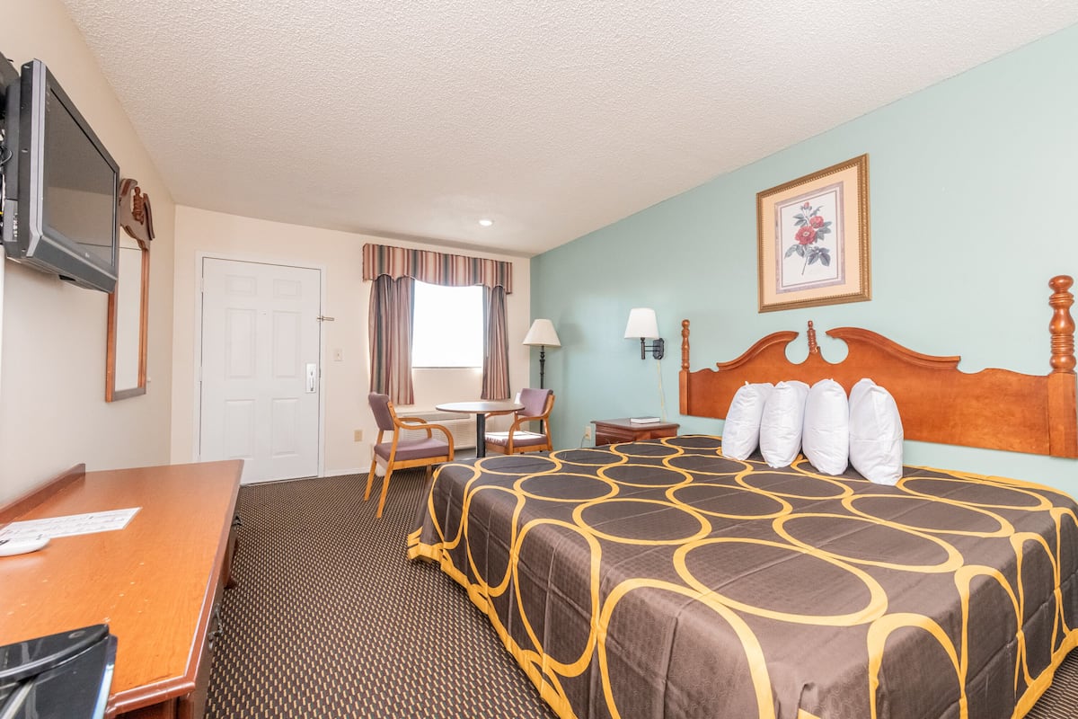 A hotel room with a large bed, a desk, a chair, a television, and a window with curtains.