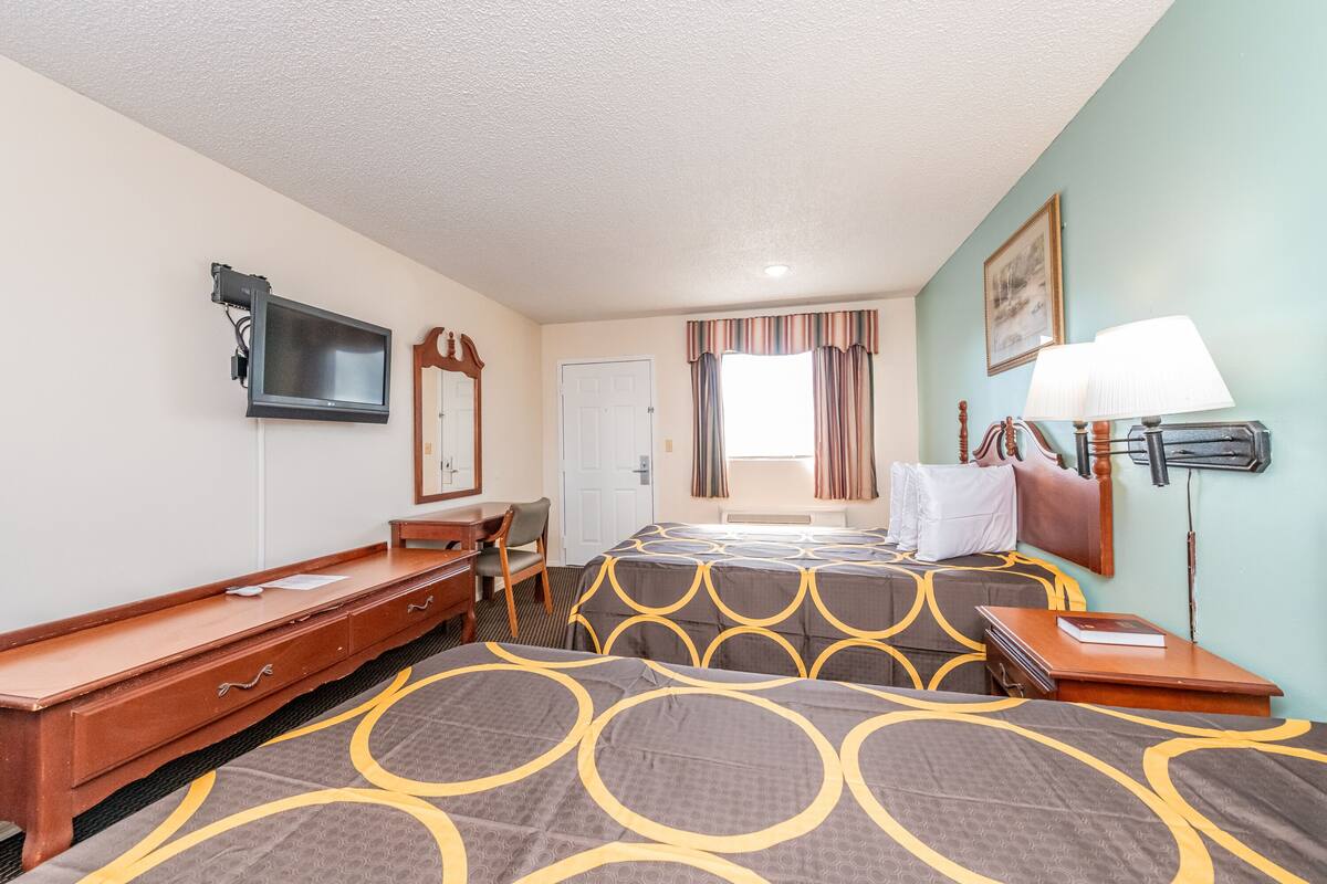 A hotel room with a bed, a desk, a chair, a TV, and a lamp.