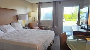A hotel room with a large bed, a desk with a television, a chair, and a window with curtains.