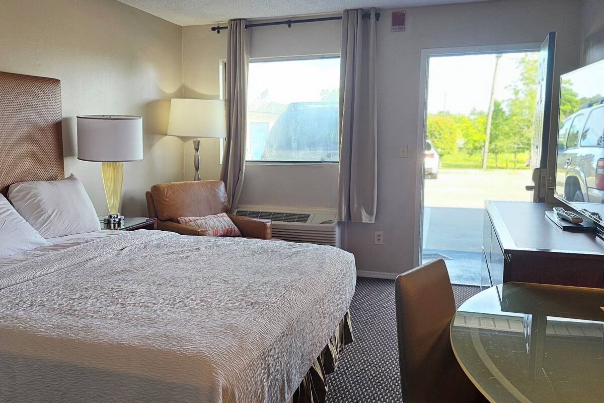 A hotel room with a large bed, a desk with a television, a chair, and a window with curtains.