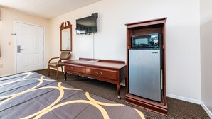 A hotel room with a bed, a wooden dresser, a television, and a microwave.