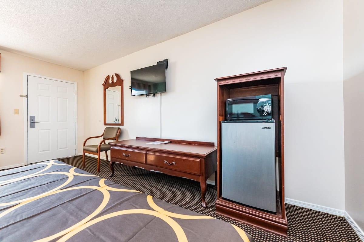 A hotel room with a bed, a wooden dresser, a television, and a microwave.