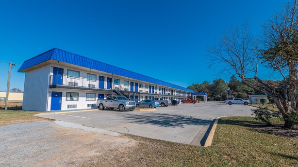 A motel with a blue roof and white walls, featuring a parking lot with several cars.
