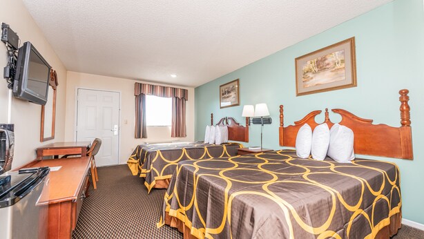 A hotel room with two beds, a desk, a television, and a window with curtains.
