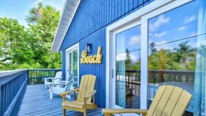 En træterrasse med to Adirondack-stole og en glasdør med et skilt, hvor der står 'Beach'.