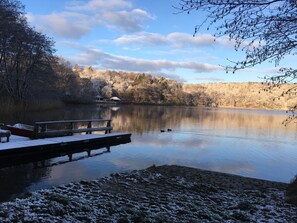 Un lago tranquilo con un muelle de madera y un edificio pequeño al fondo.