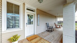 Un porche avec un plancher en bois, un paillasson, une porte et une enseigne sur laquelle on peut lire « FERME ».