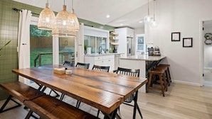 A modern kitchen with white cabinets, a wooden dining table, and pendant lights.