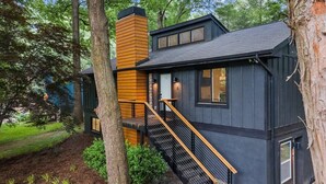A modern house with a wooden staircase leading to a deck, surrounded by trees.