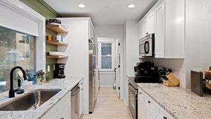 A modern kitchen with white cabinets, granite countertops, a stainless steel sink, and a microwave.