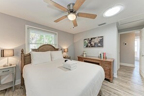 A bedroom with a large bed, a wooden headboard, a ceiling fan, a nightstand with a lamp, a dresser, and a world map on the wall. - La Cocolia located on north end of Ami. Lagoon Pool, Walk to Pine Ave. (Anna Maria)