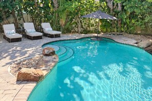 A swimming pool with lounge chairs and an umbrella.