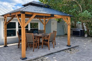 A wooden gazebo with a metal roof, surrounded by a brick patio, and a dining table with chairs. - La Cocolia located on north end of Ami. Lagoon Pool, Walk to Pine Ave. (Anna Maria)