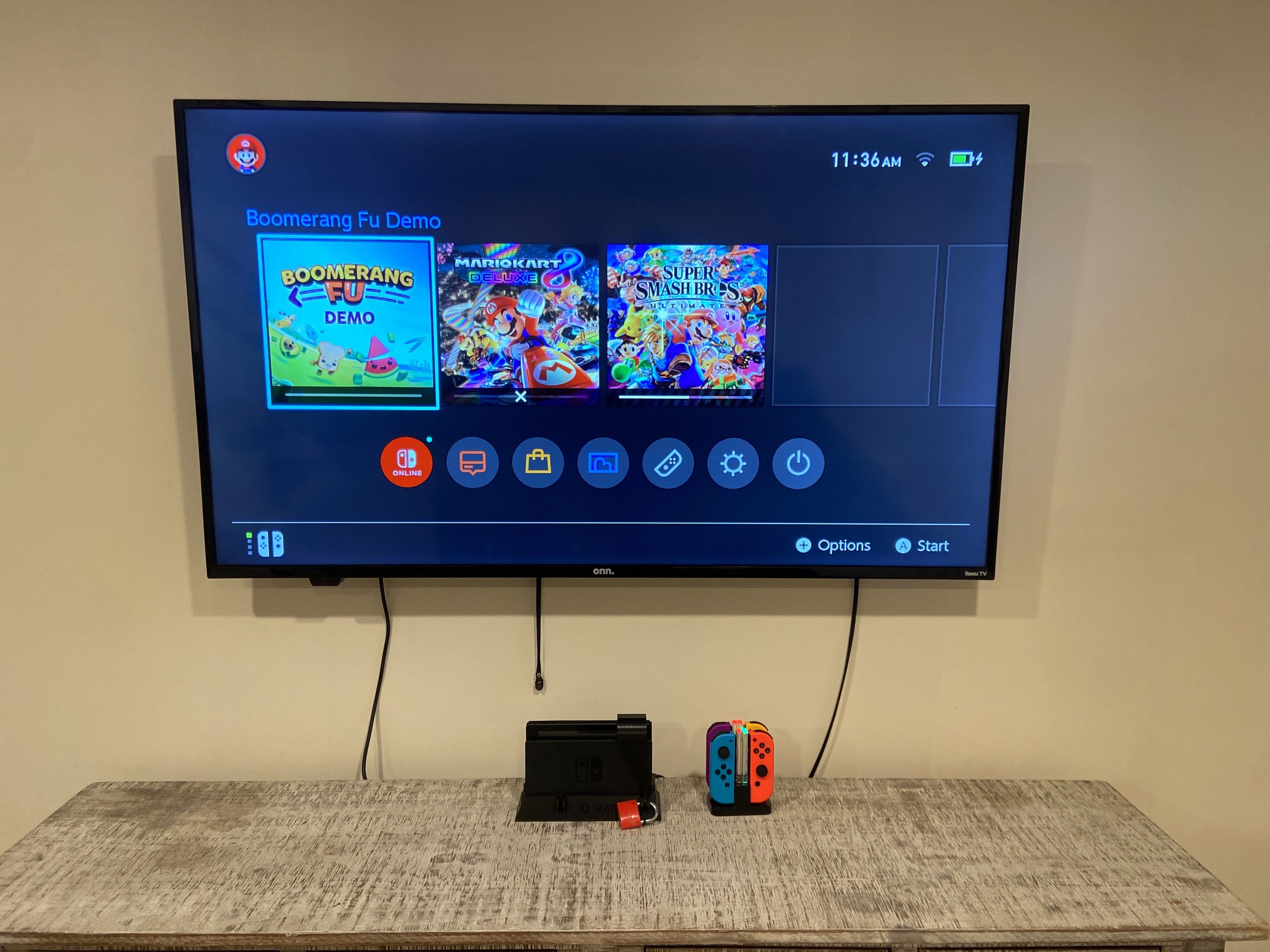 Un téléviseur affiche un menu de jeu proposant les options suivantes : « Boomerang Fu Demo », « Mario Kart Deluxe » et « Super Smash Bros. Ultimate ».