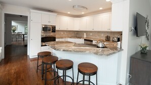 Une cuisine moderne avec des meubles blancs, un îlot en granit doté de tabourets et des appareils électroménagers intégrés.