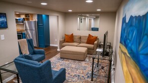 A modern living room with a sofa, two armchairs, a coffee table, and a patterned rug. A kitchen with a refrigerator and microwave is visible in the background. - Charming 2-Bedroom Apartment – Minutes to Downtown & MSU! (Bozeman)