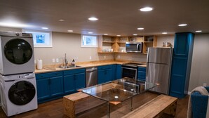 A modern kitchen with blue cabinets, stainless steel appliances, and a glass-top dining table. - Charming 2-Bedroom Apartment – Minutes to Downtown & MSU! (Bozeman)