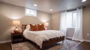 A bedroom with a wooden bed, two bedside lamps, a patterned rug, and a window with curtains. - Charming 2-Bedroom Apartment – Minutes to Downtown & MSU! (Bozeman)