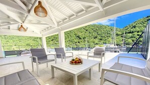 A covered outdoor seating area with white furniture and a table with fruit. - Marina Beach 1, entre la plage et la marina (Anse Marcel)