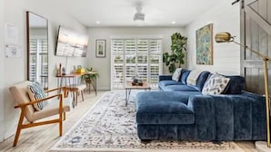 A modern living room with a blue sofa, wooden chair, and a large window with blinds. - Modern Beach House, 1 block from beach! (Holmes Beach)