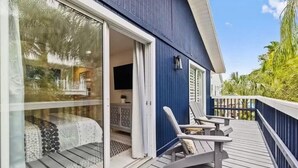 A wooden deck with two lounge chairs and a glass door leading to a room with a bed and a TV. - Modern Beach House, 1 block from beach! (Holmes Beach)