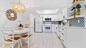 A modern kitchen with white cabinetry, a dining table with chairs, and a hanging light fixture. - Modern Beach House, 1 block from beach! (Holmes Beach)