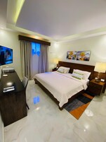 A hotel room with a bed, a desk, a television, and artwork on the wall.