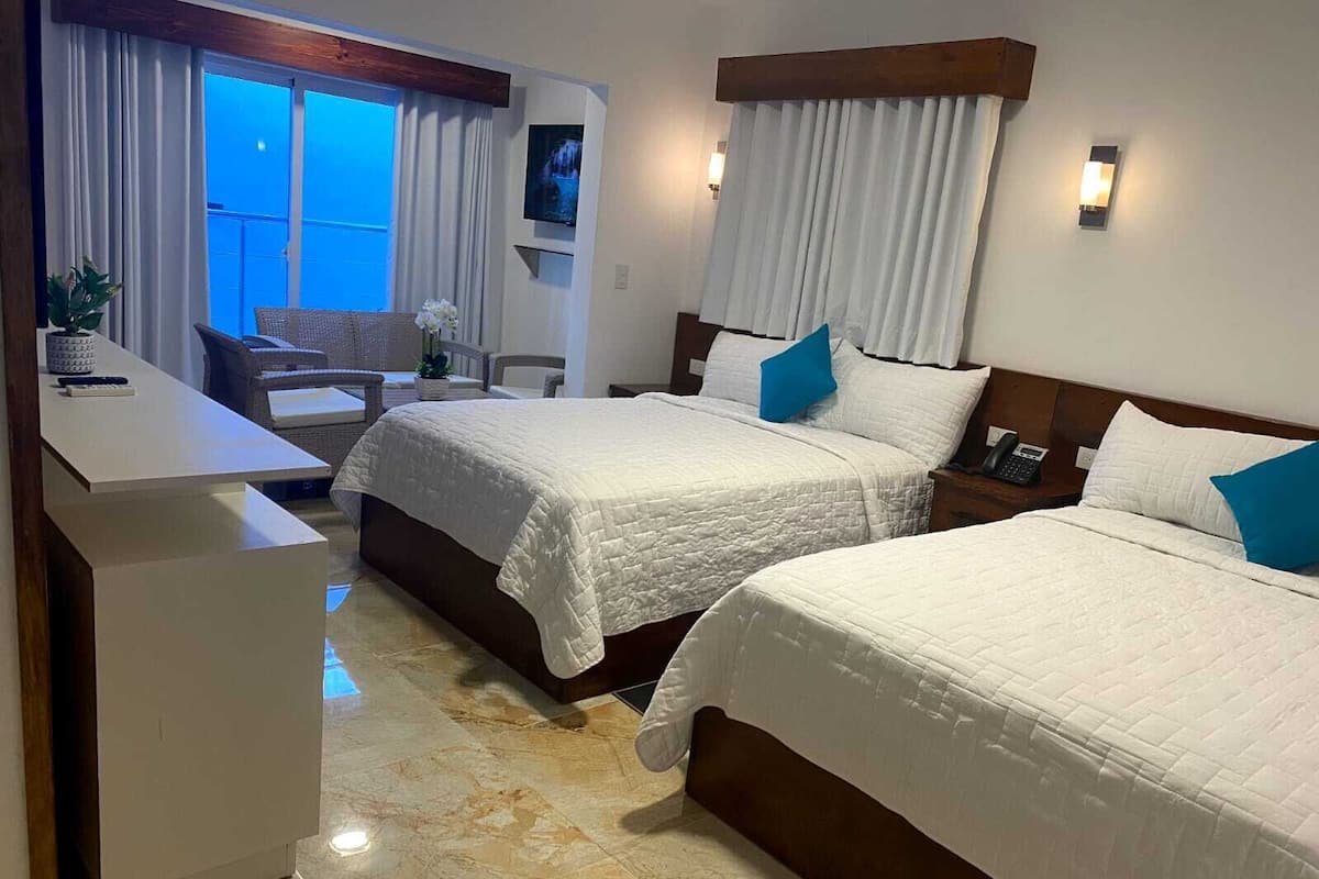 Habitación de hotel con dos camas, un escritorio y vistas al exterior.
