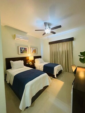 A hotel room with two beds, a ceiling fan, an air conditioning unit, a desk, and a chair. - Halibut Hotel  (Villa Hermosa)