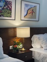 A hotel room with two beds, a nightstand with a lamp, and framed artwork on the wall.