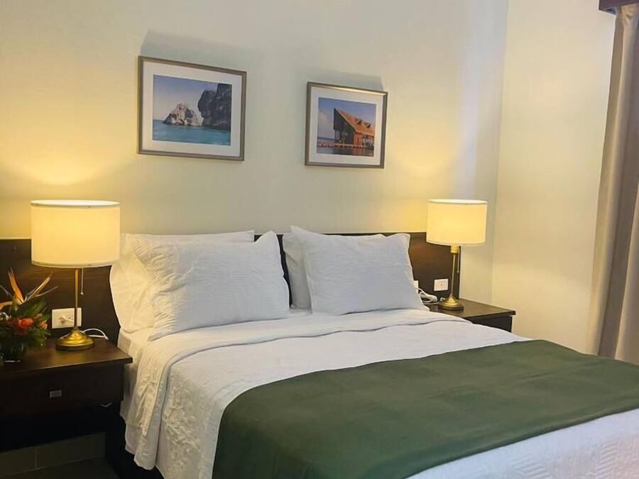 A hotel room with a bed, two bedside lamps, an air conditioning unit, and two framed pictures on the wall.