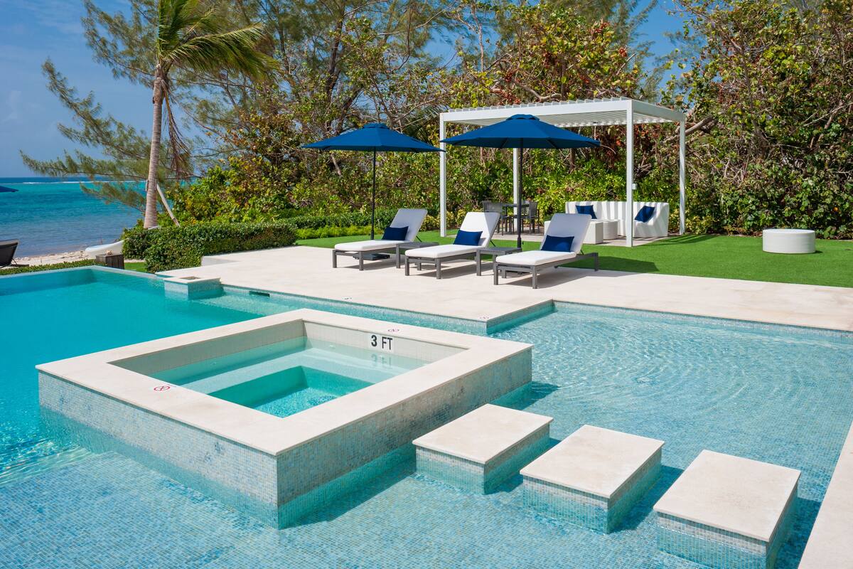 Un área de piscina con sillones de descanso, sombrillas y un pequeño jacuzzi.