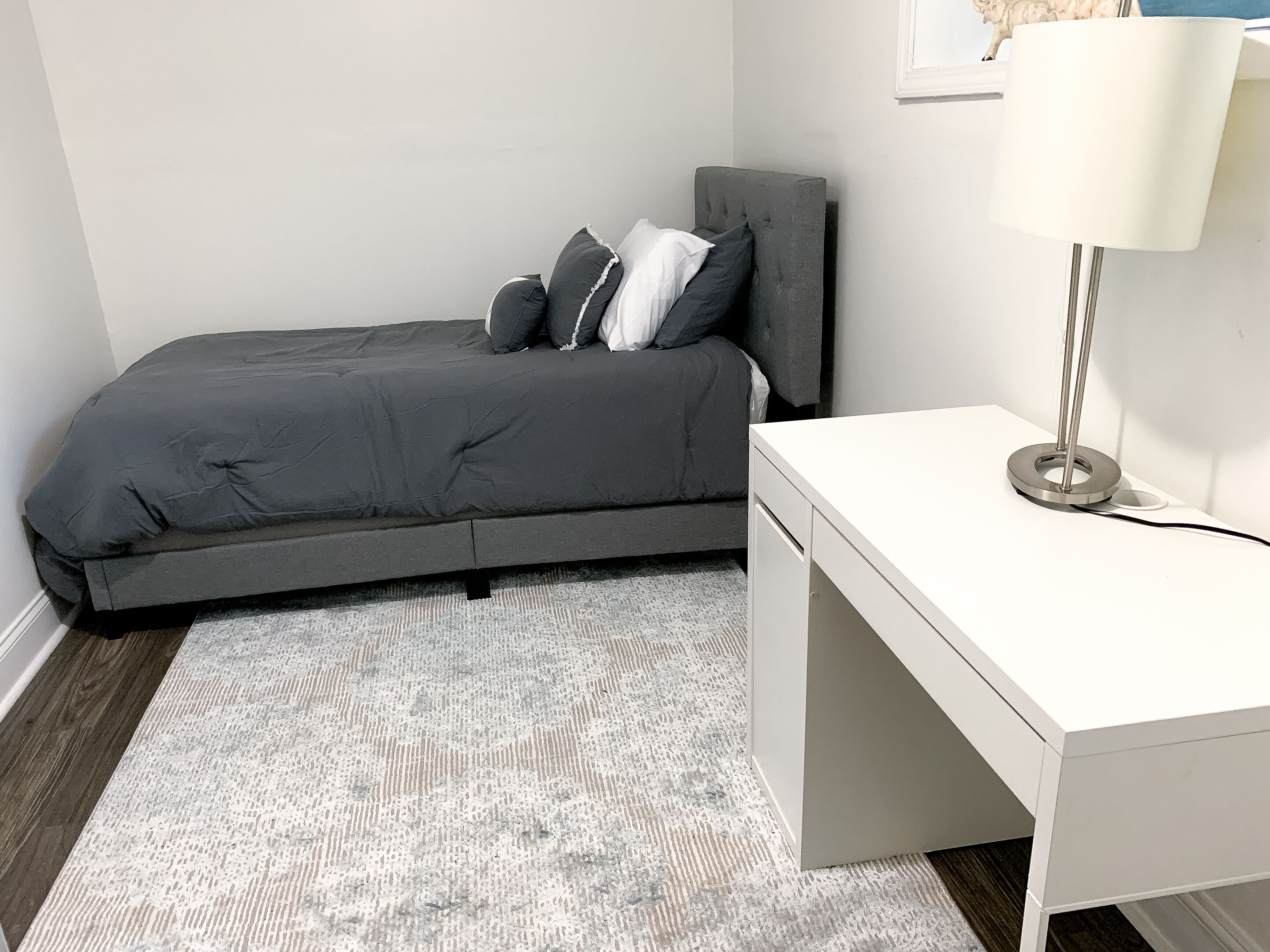 A compact bedroom with a bed, bedside table, and a desk.