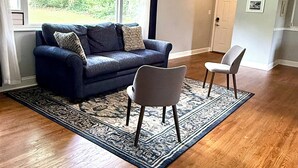 Un salón con un sofá azul oscuro, un tapete estampado, un ventilador de techo y vistas amplias por las ventanas.